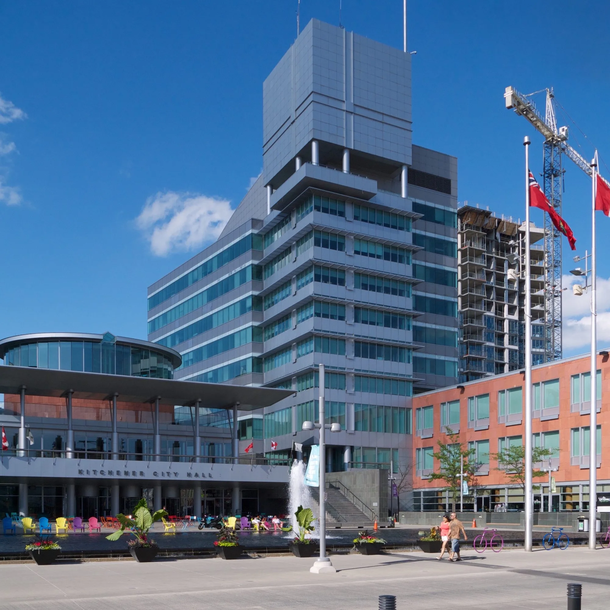 Kitchener City Hall, a modern glass and metal tower above the entrance canopy and public square, with flags and a fountain in front